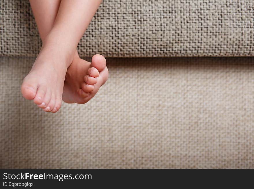 Children`s legs close-up hanging from the sofa in the room. Baby toes while baby is sitting on the armchair