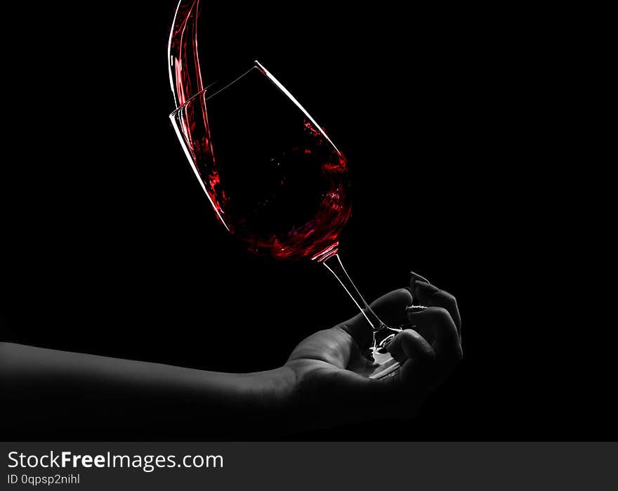 A glass of wine in hand, red wine pours into a glass, an over black background. A glass of wine in hand, red wine pours into a glass, an over black background