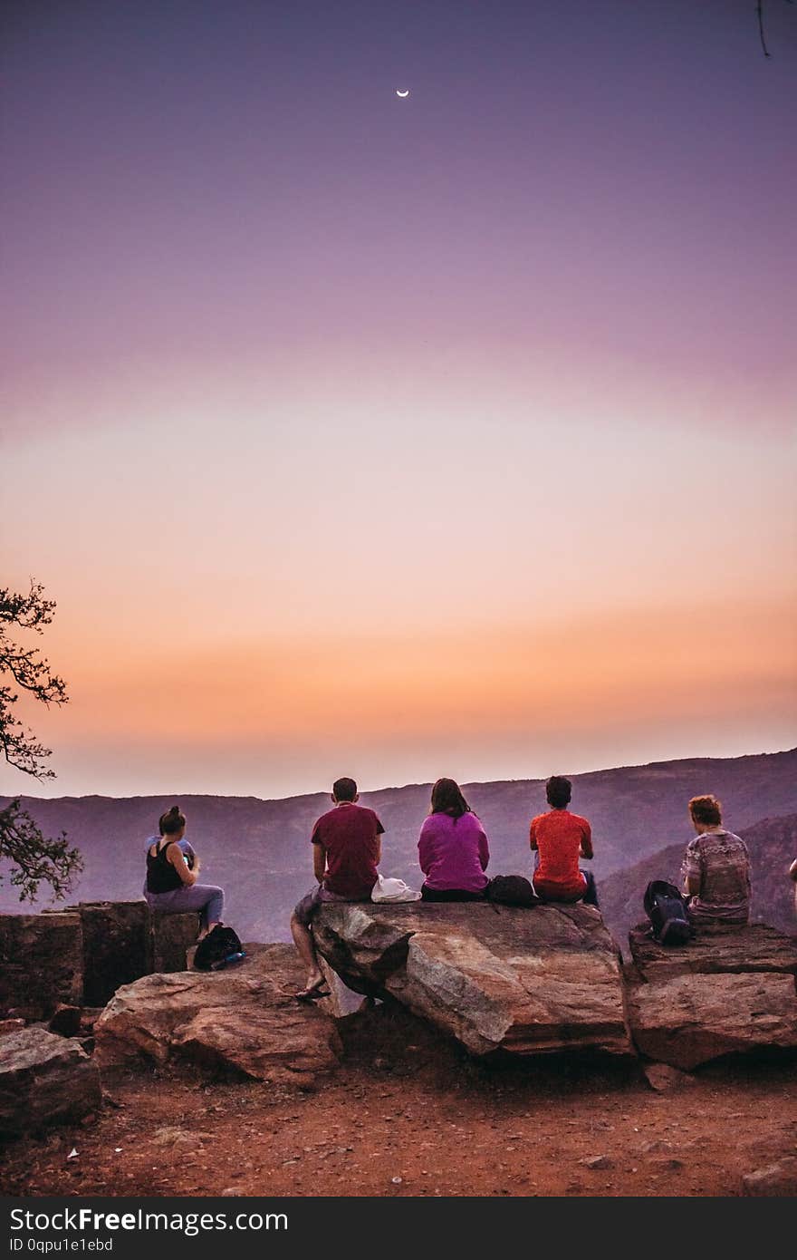 A Group Of Young Travelers Sitting On Top Of A Mountain And Watching A Beautiful View Of The Canyon