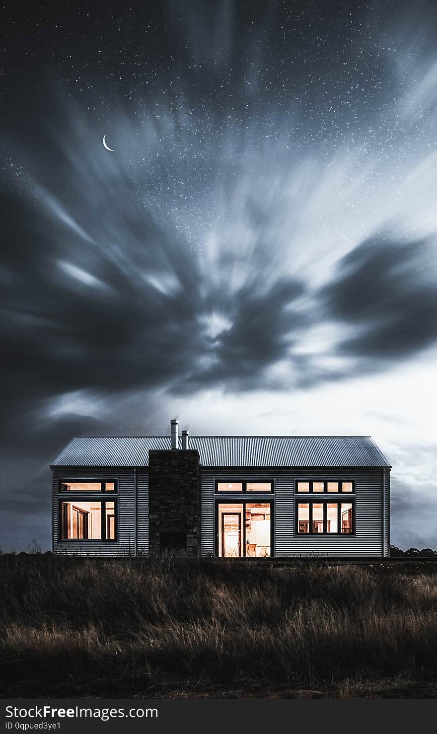 A mysterious house with the lights on  in a dark field with breathtaking moving clouds and a half moon - Perfect for a fantasy horror concepts