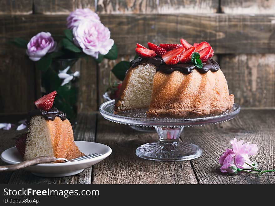 Summer cake with chocolate glaze and fresh strawberries on top on rustic wooden table, close up, selective focus