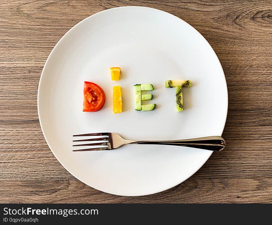 Word DIET made of sliced vegetables in plate with measuring on wood background