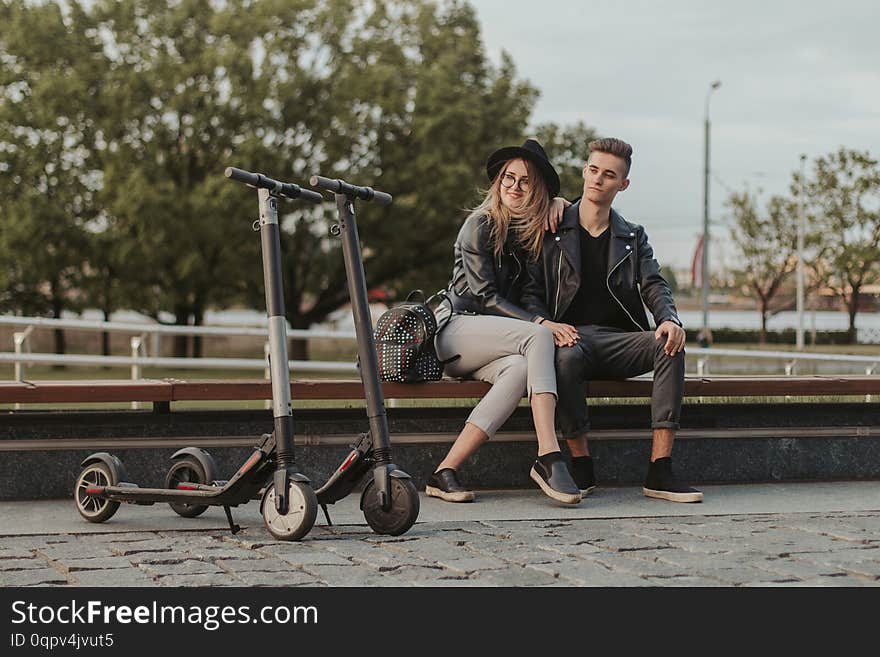 Happy trendy couple is chilling on the bench at city park with their scooters. Happy trendy couple is chilling on the bench at city park with their scooters.