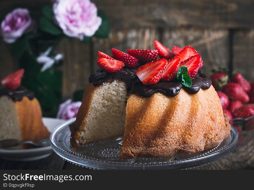 Summer cake with chocolate glaze and fresh strawberries on top on rustic wooden table, close up, selective focus