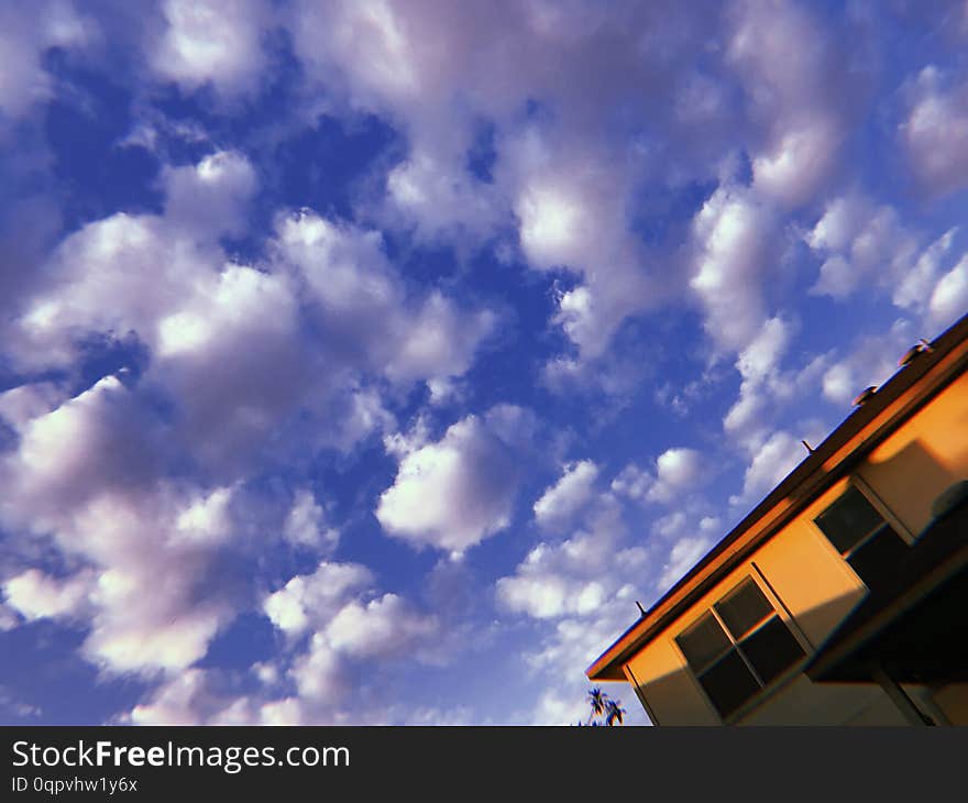 Puffy white clouds scudding across a blue sky on a sunny summer day in suburbia. A house from the suburbs. Puffy white clouds scudding across a blue sky on a sunny summer day in suburbia. A house from the suburbs.