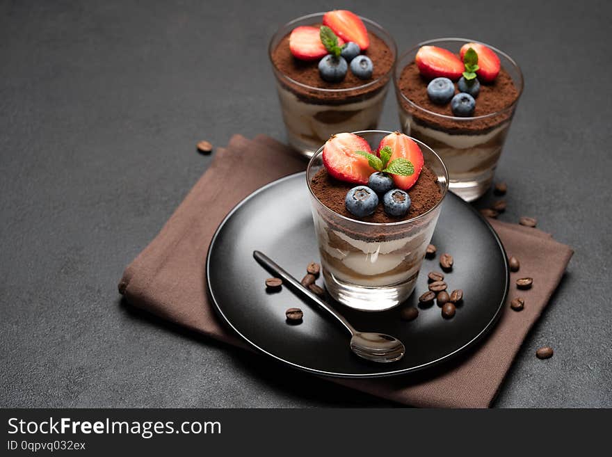 Classic tiramisu dessert with blueberries and strawberries in a glass on stone serving board on dark concrete background or table