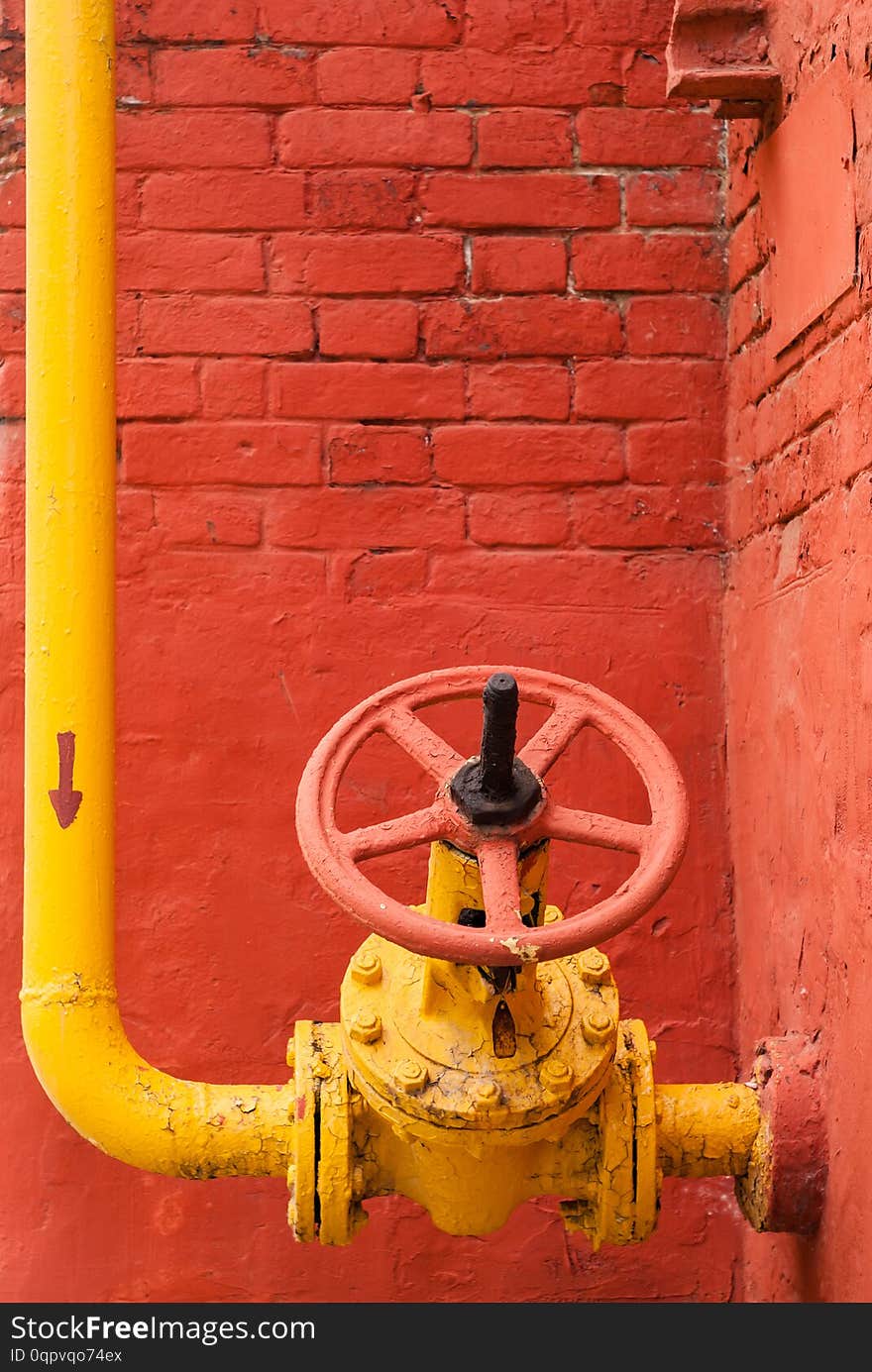 Yellow industrial gas pipeline with elbow and isolation valve with rotary handle against the background of a red brick wall. Yellow industrial gas pipeline with elbow and isolation valve with rotary handle against the background of a red brick wall