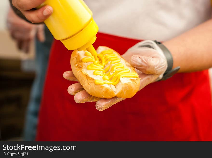 Hands of street chef puts mustard on a hot dog bun close up. Hands of street chef puts mustard on a hot dog bun close up