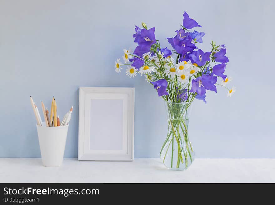 Mockup with a white frame and summer blue flowers in a vase on a light blue background