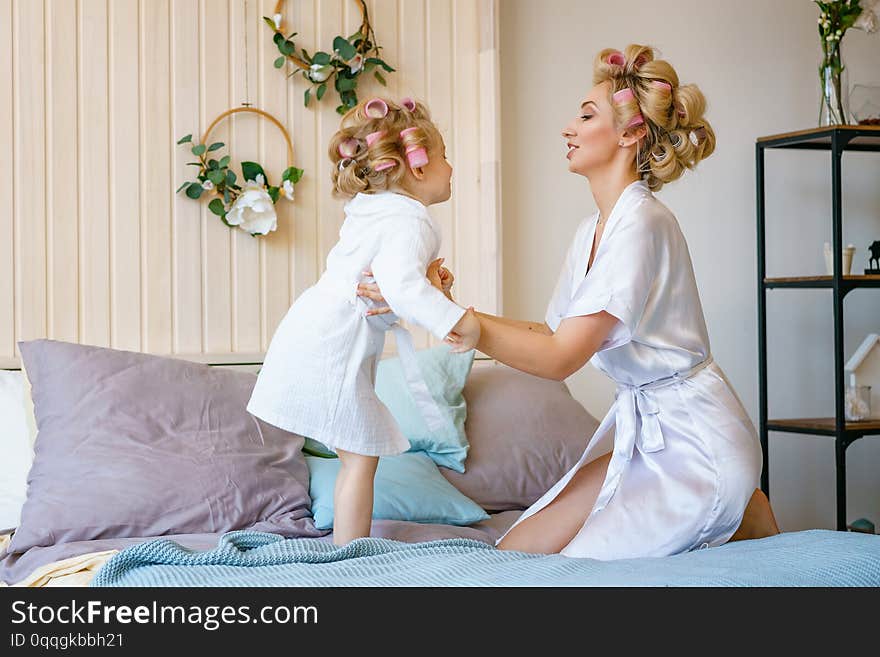 Happy mom and daughter having fun on the bed in dressing gowns.