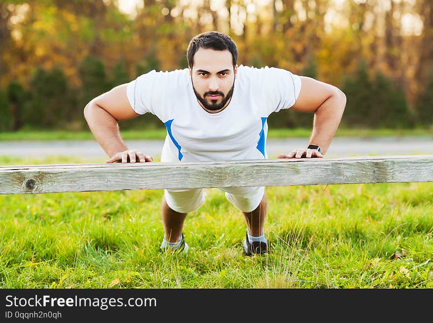 Portrait sporty man 30s in sportswear doing push-ups in green park