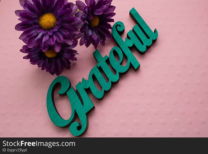 Purple flowers and a wooden painted word laid on a pink textured background. Purple flowers and a wooden painted word laid on a pink textured background.