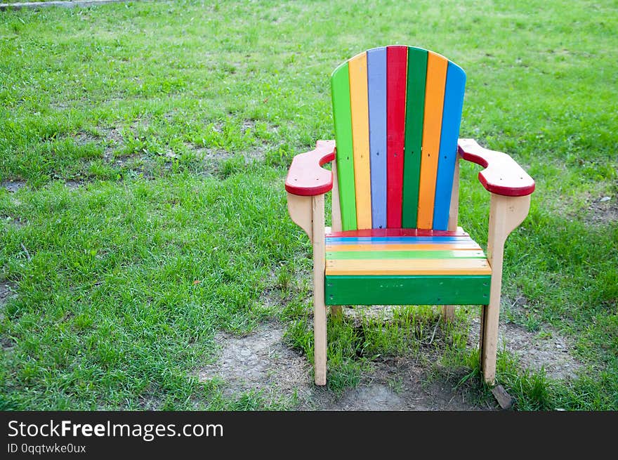 A multi-colored wooden chair on the playground. On the background of green grass. Summer