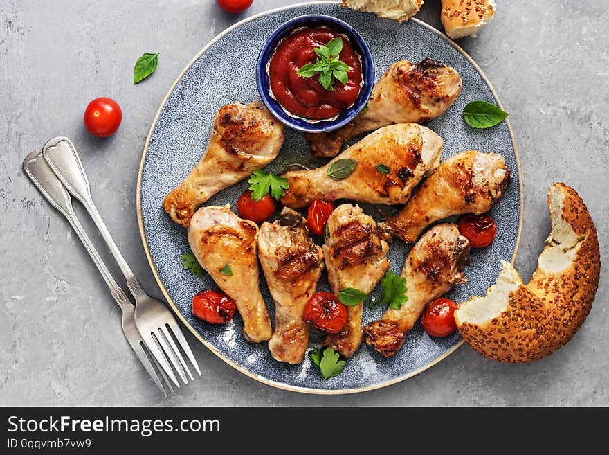 Closeup of fried chicken drumstick with tomatoes, ketchup and fresh bagel bread over gray background. Top view, flat lay.