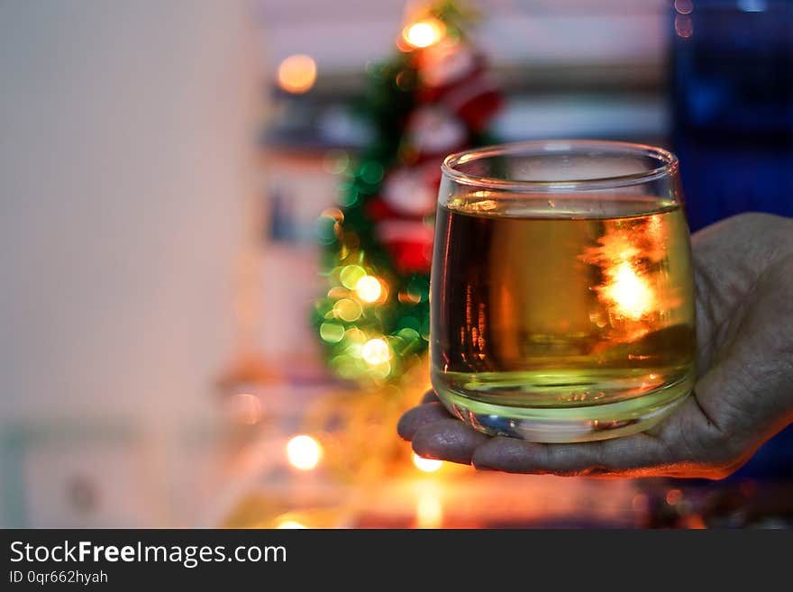 A glass of alcohol rum held in hand with background blurred bokeh lights.