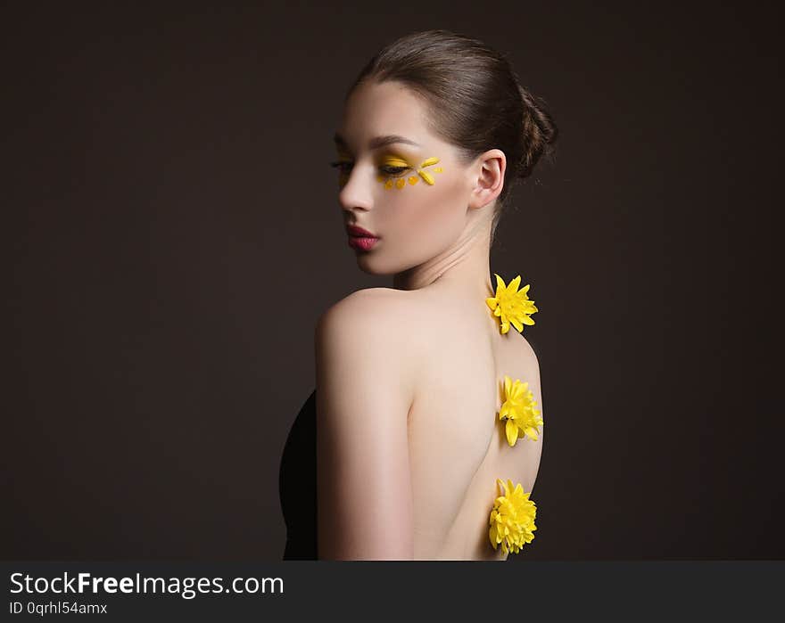 Young Woman Spa. Yellow Flowers Along Her Back, Face And Body In The Shade. Back View. Dark Background