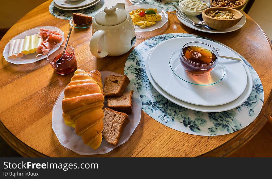 Breakfast table with variety of foods including cereals, cheese, yogurt, scrambled eggs, fruit, croissant and drinks such as tea, coffee and orange juice. Breakfast table with variety of foods including cereals, cheese, yogurt, scrambled eggs, fruit, croissant and drinks such as tea, coffee and orange juice.