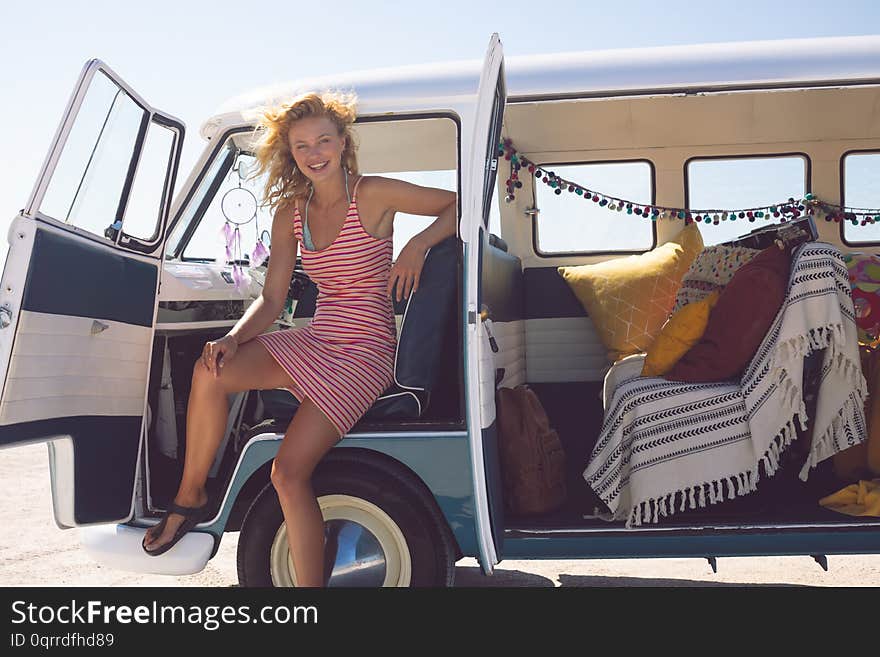 Front view of happy Caucasian woman looking at camera while sitting in camper van at beach