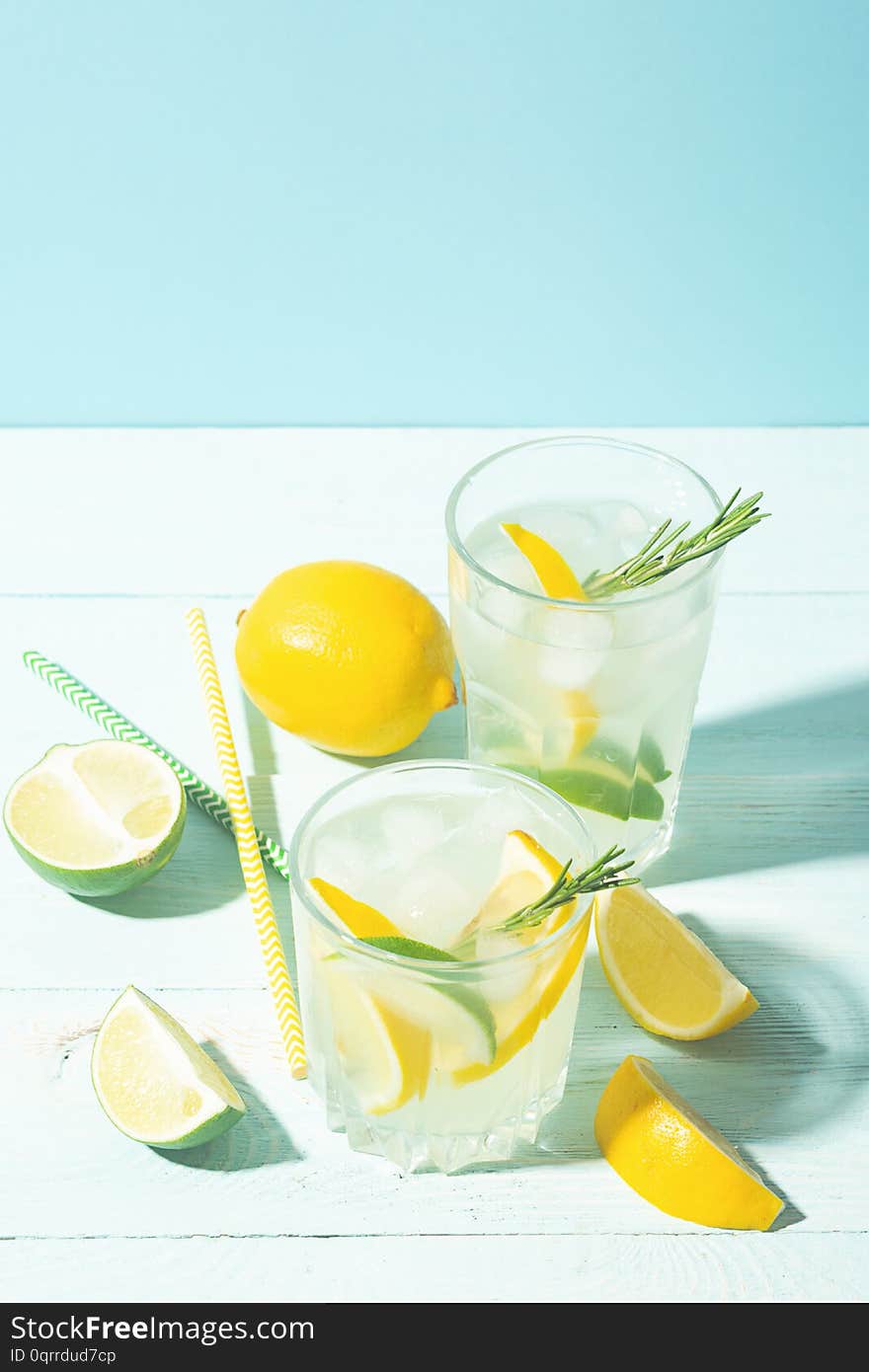 A drink of lemon and lime in an elegant glass on a blue background with bright sunshine. Summer cocktail or mojito. Vertical frame. Copy space. Selective focus.