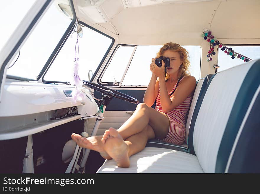 Front view of beautiful Caucasian woman taking photo with digital camera in camper van at beach