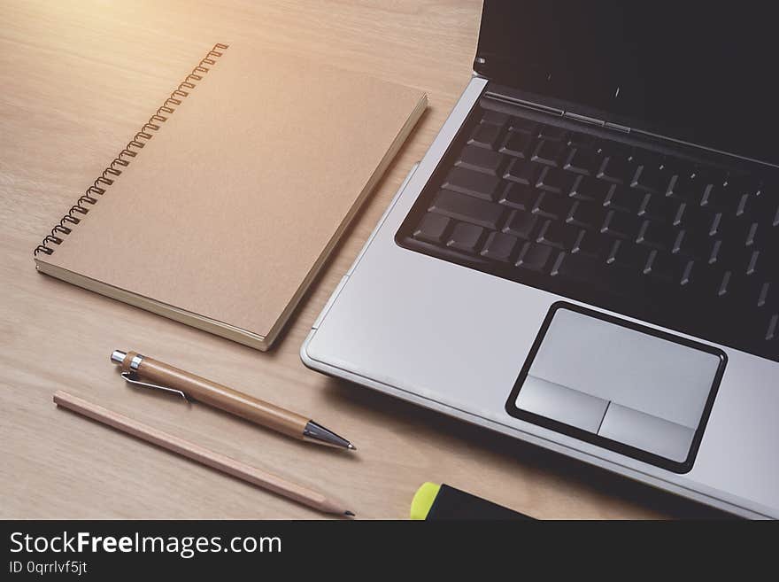 Workspace with diary or notebook and laptop, pen, pencil, hightlight pen, metal clip on wooden background