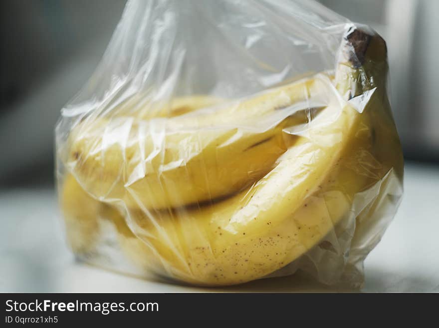 A bunch of almost ripe bananas wrapped in a transparent plastic bag on white table surface