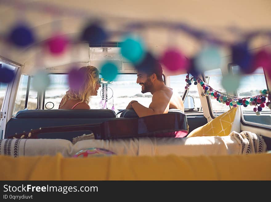 Rear view of happy Caucasian couple talking with each other in camper van at beach