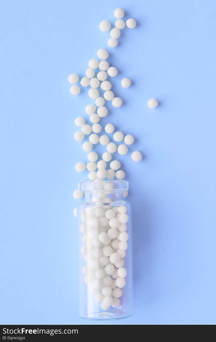 Close up homeopathic globules and glass bottle on blue background. Alternative Homeopathy medicine herbs, healtcare and pills