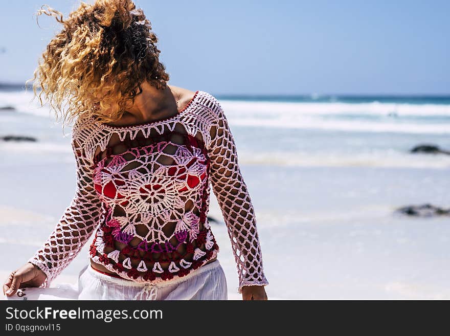 Beautiful woman with hand made dress enjoy the beach in summer vacation - outdoor leisre activity in tropical place - blue ocean and sky in background - curly hair moved by the wind