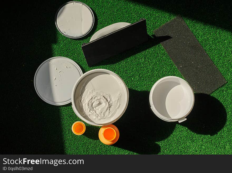 A can of white and yellow paint stands on the grass