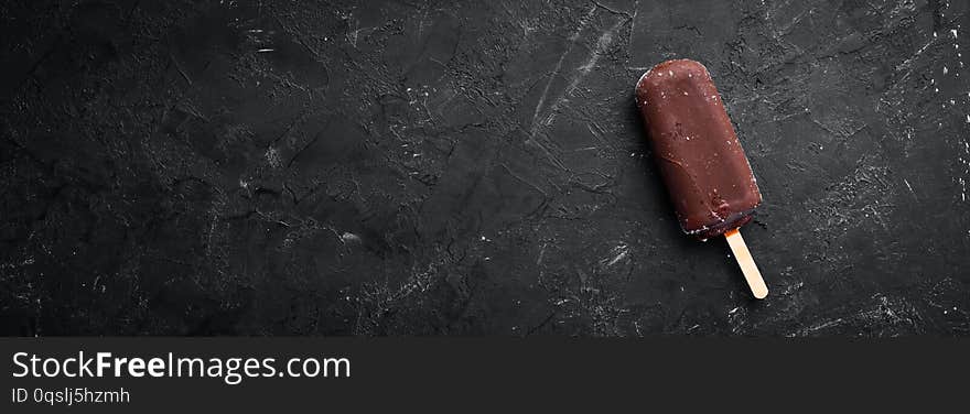 Chocolate ice cream on a stick. On a black background.