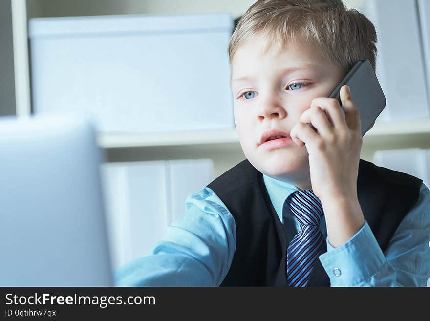 Young confident executive businessman boss boy in office talks on the phone sitting at the desk with laptop.