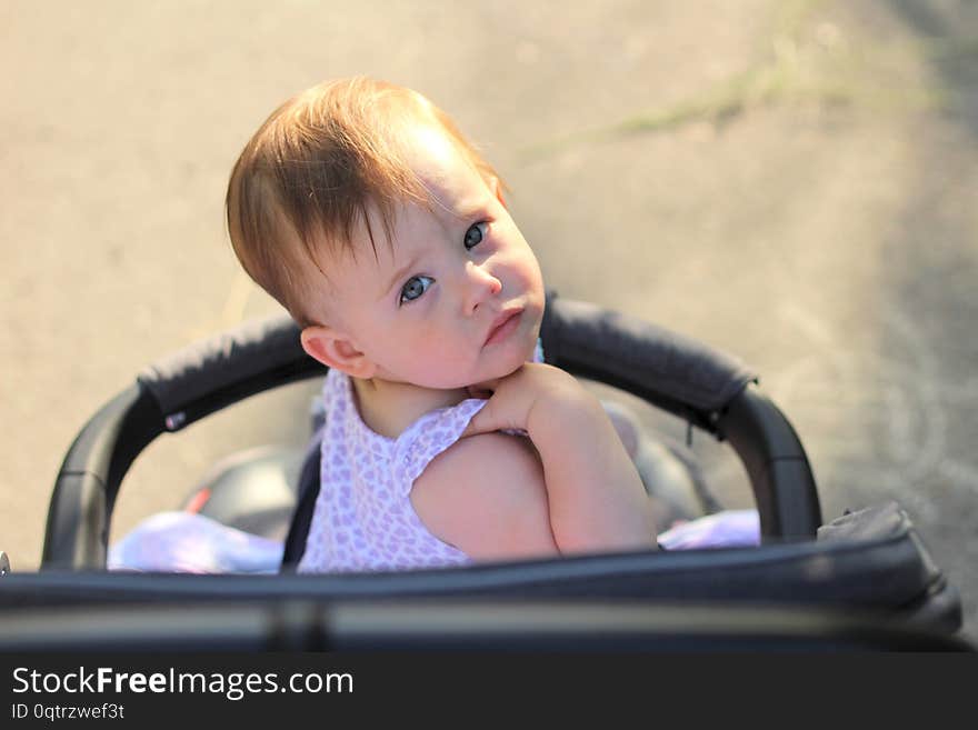 little, beautiful, smiling, cute redhead baby in a sleeveless shirt in a pram out-of-doors drops hands down and looking back