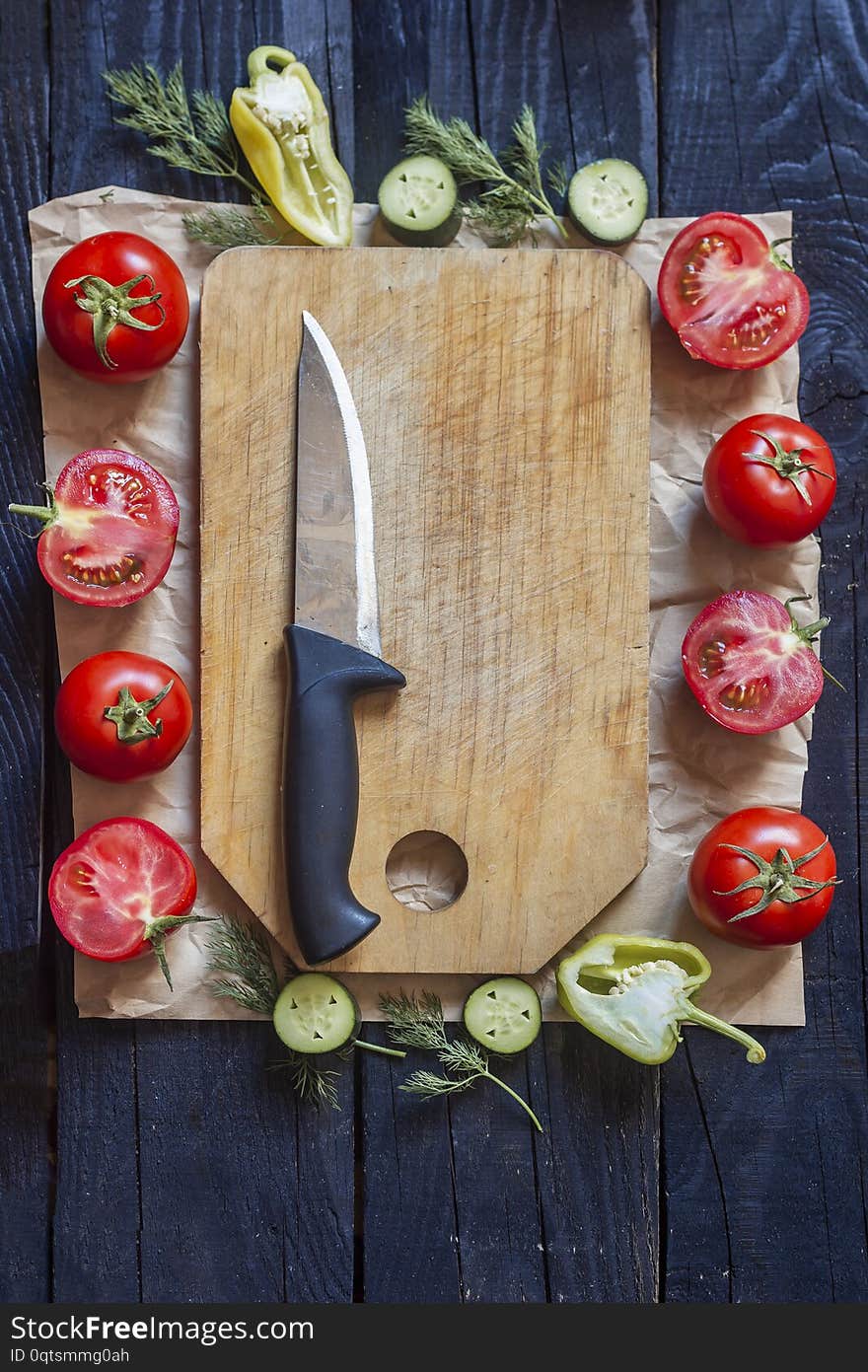 Salad ingredients. Fresh raw vegetables on wood. Cutting board with a kitchen knife. Cucumbers, tomatoes, peppers, greens. Salad ingredients. Fresh raw vegetables on wood. Cutting board with a kitchen knife. Cucumbers, tomatoes, peppers, greens