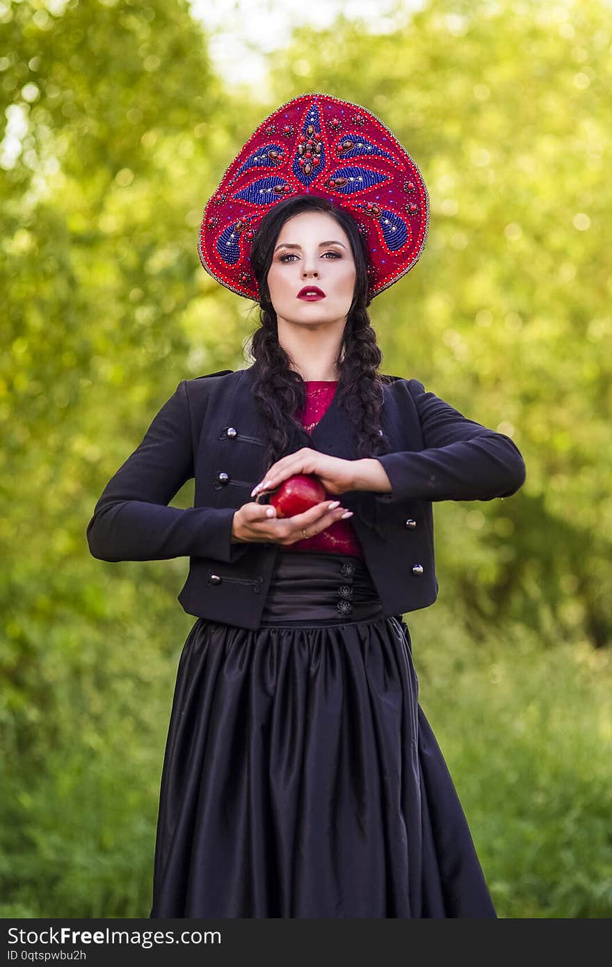 Fashion Brunete Woman In Russian Style Kokoshnik Outdoors Against Nature Background. Posing With Apple