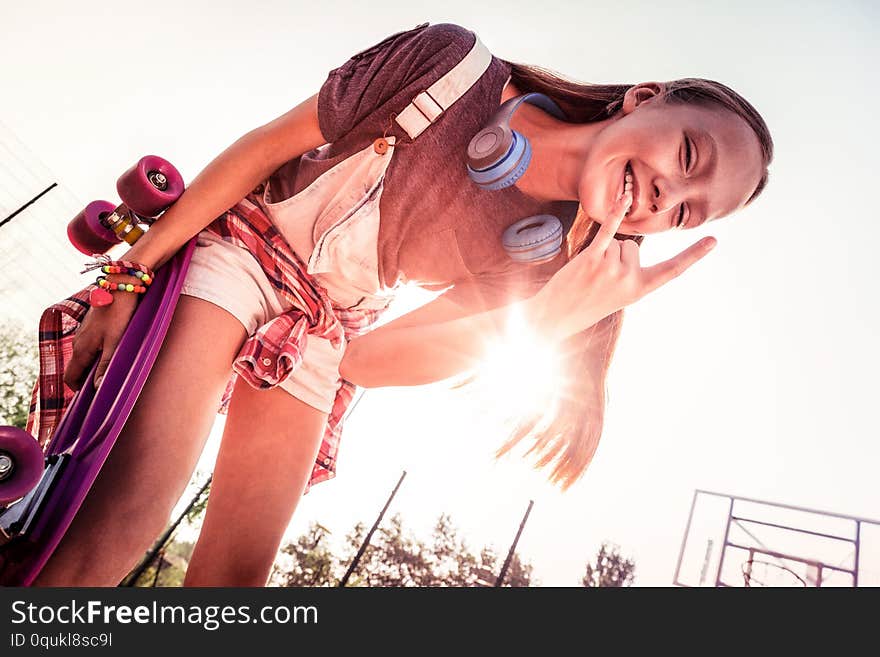 Warm summer holidays. Beaming long-haired girl being in great mood while staying outside while wearing headphones