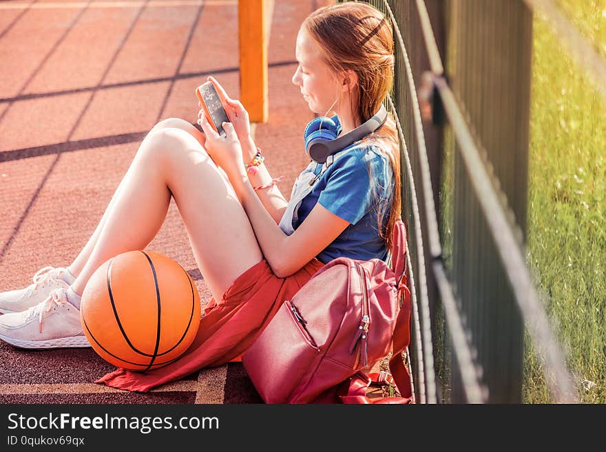 Focused long-haired girl sitting on a basketball playground