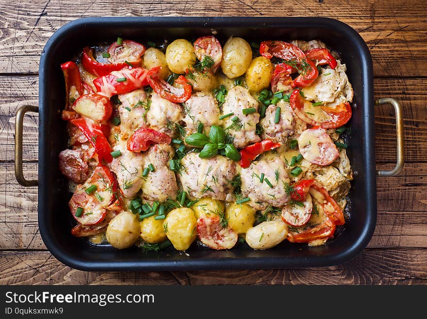 Baked chicken thighs, potatoes and vegetables in a baking tray on a wooden table