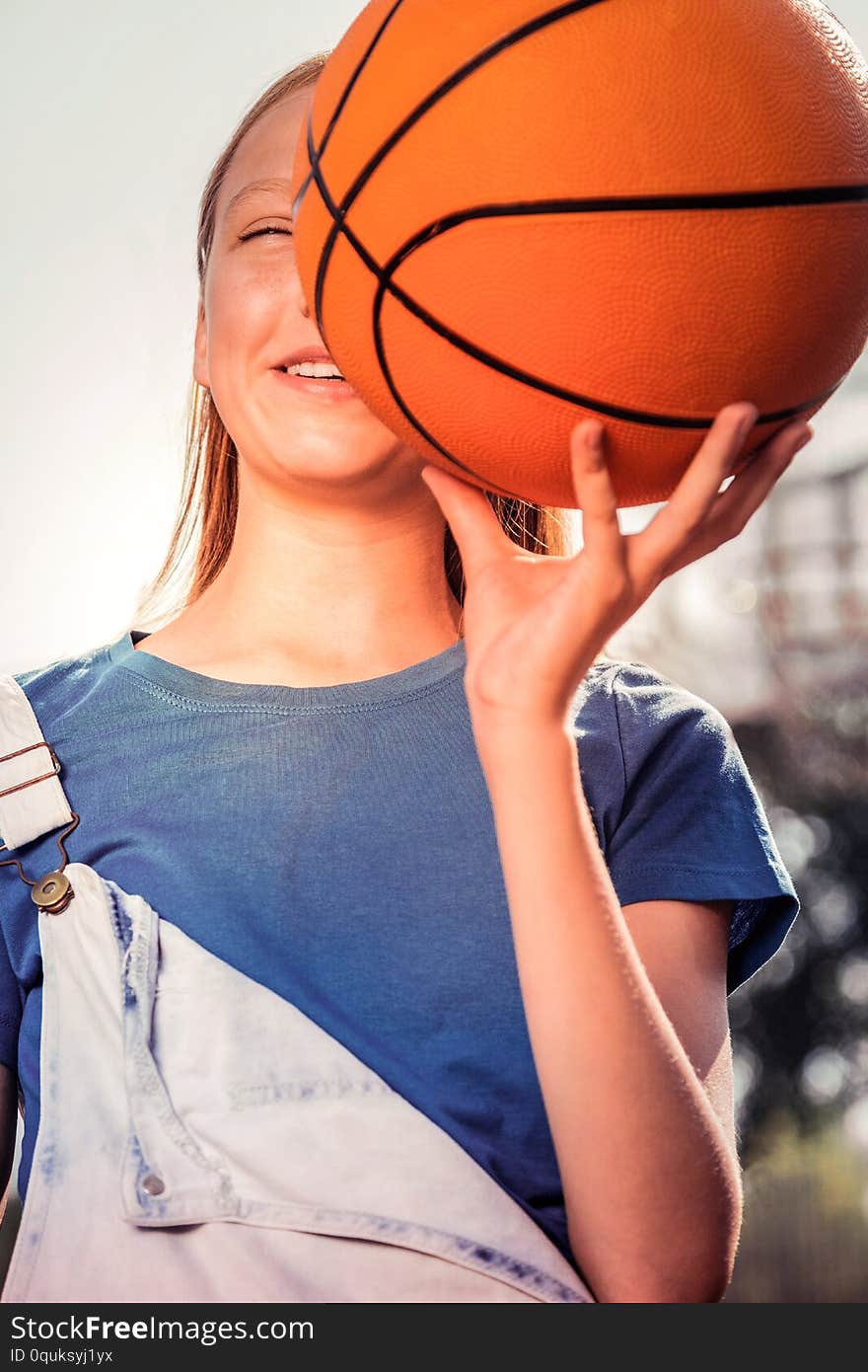 Holding basketball ball . Cheerful young sportive lady in blue t-shirt carrying ball near her face while having fun in a park