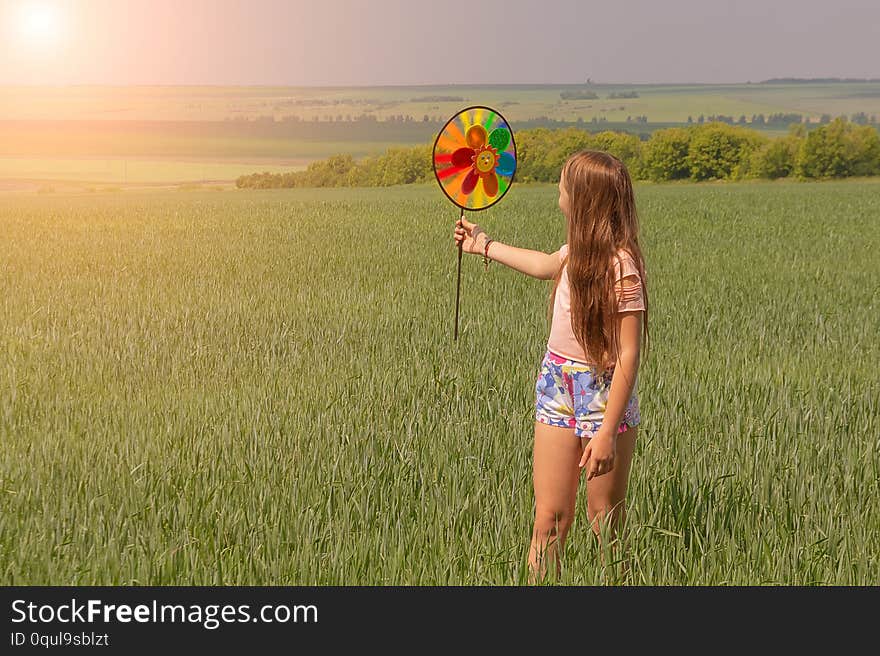 A happy girl with long hair is holding a colored windmill toy in her hands