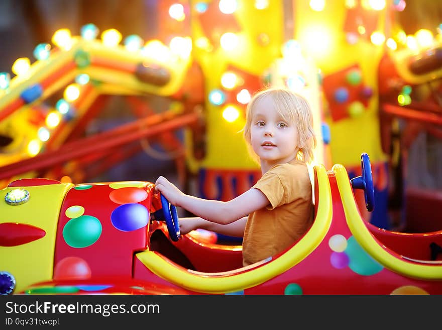 Little boy having fun on attraction in public park. Child riding on a merry go round at summer evening. Attraction, planes, cars, illumination, fun... Entertainment industry