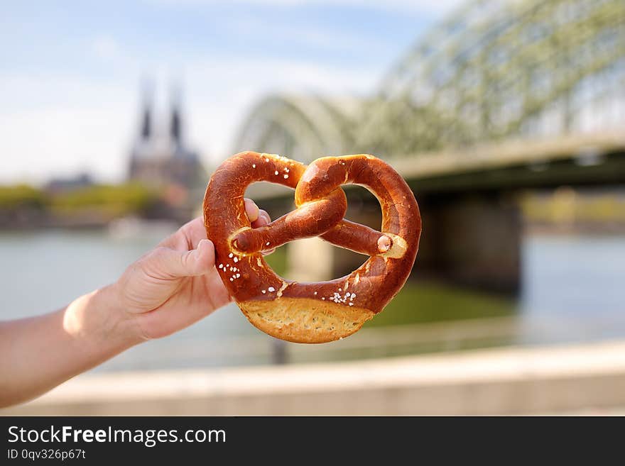 Traditional germany food pretzel on background of embankment of Rhine and Cologne Cathedral, Hohenzollern Bridge in Koel, Germany. Sightseeing of Germany