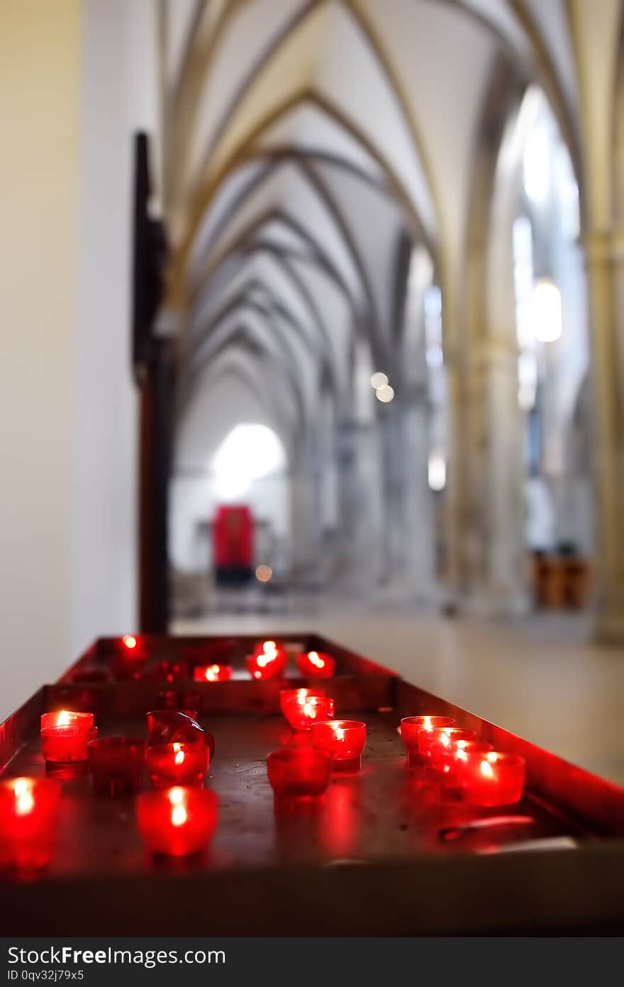 Close-up photo of church candles in red transparent chandeliers in Church