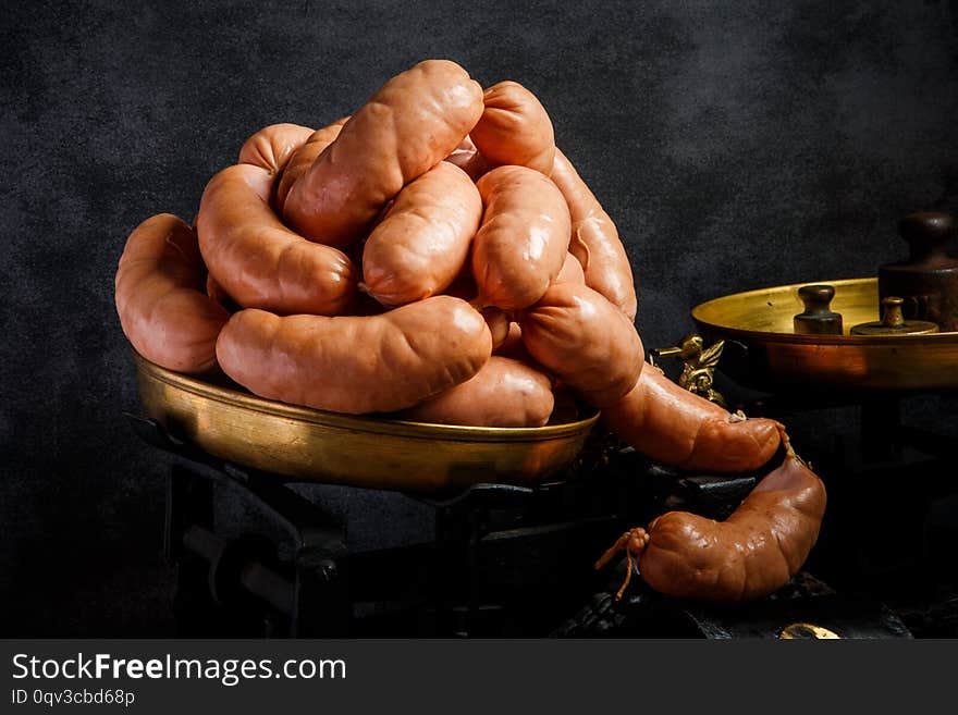 big bunch of raw short thick wieners with natural casings rolled in spiral on antiquarian scales over black background. big bunch of raw short thick wieners with natural casings rolled in spiral on antiquarian scales over black background