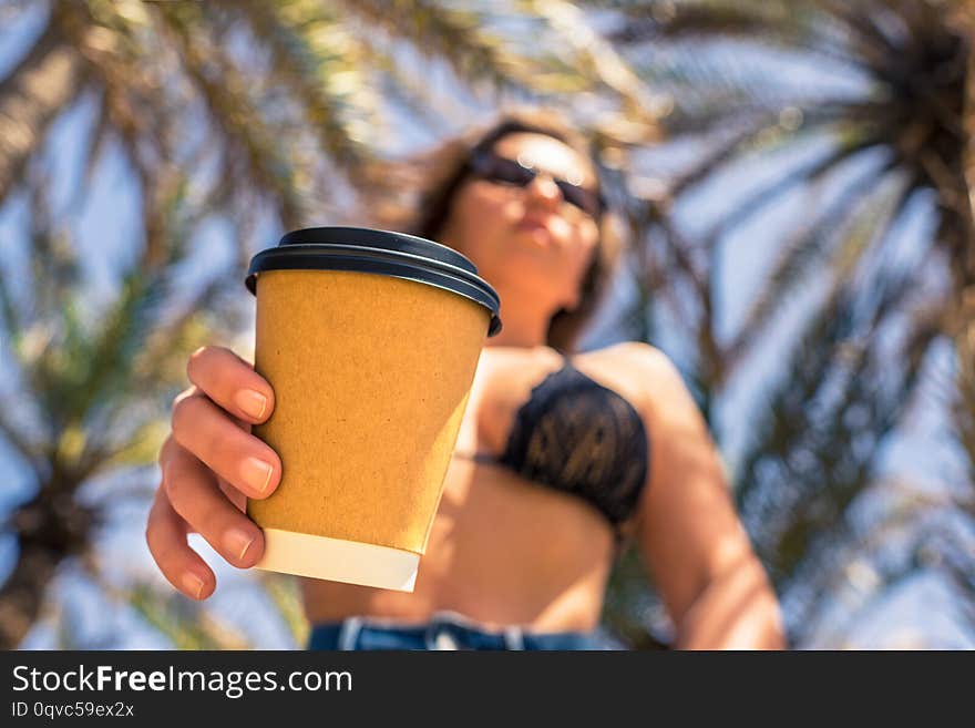 Woman`s Hand With Paper Cup Of Coffee On The Palm Trees Background.