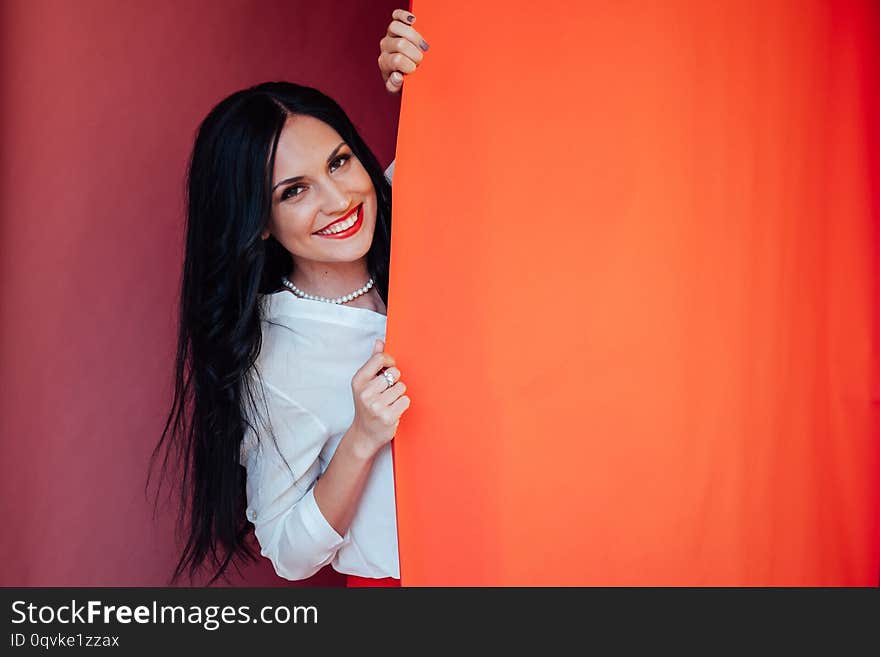 Portrait of happy satisfied beautiful brunette young woman with makeup in denim casual style standing and looking at camera with toothy smile. indoor studio shot, isolated on red background.