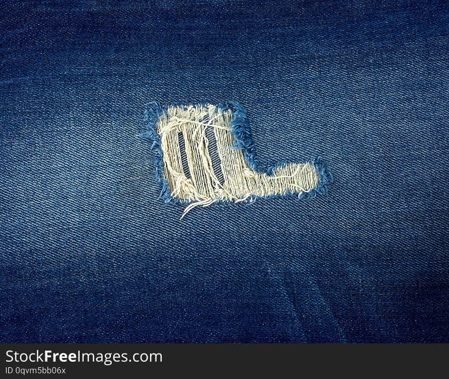 fragment of blue jeans fabric with a hole, full frame