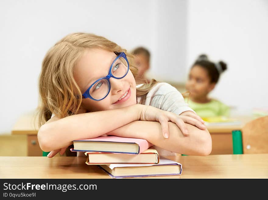 Girl in classroom at desk leaning head on books.