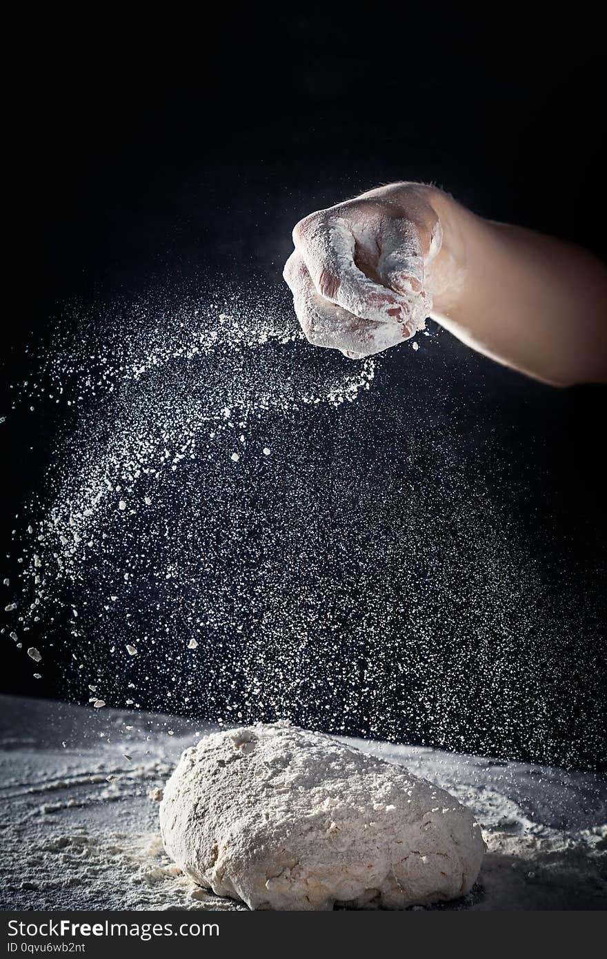 Chef prepares the dough with flour. male sprinkling flour over dough on table on dark background. Vertical. Copy space. Conceptn of flying food. Gluten free dough for pasta, bakery or pizza