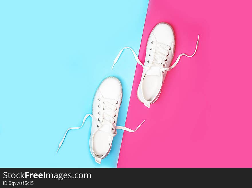 White sneakers are lying on bright neon color blue pink background.